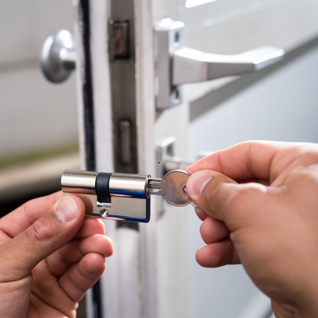 Handen plaatsen een nieuwe cilinder in het slot van een witte deur met een sleutel.