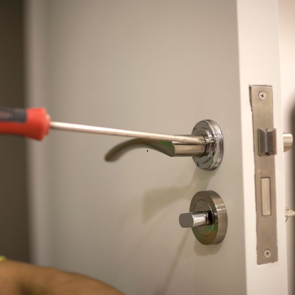 Schroevendraaier die een deurklink vastdraait op een witte deur.