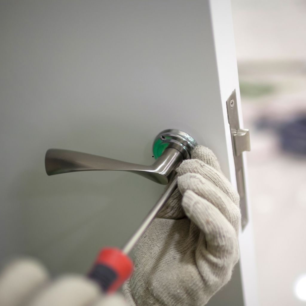 Monteur draait een deurklink vast met een schroevendraaier op een witte deur.