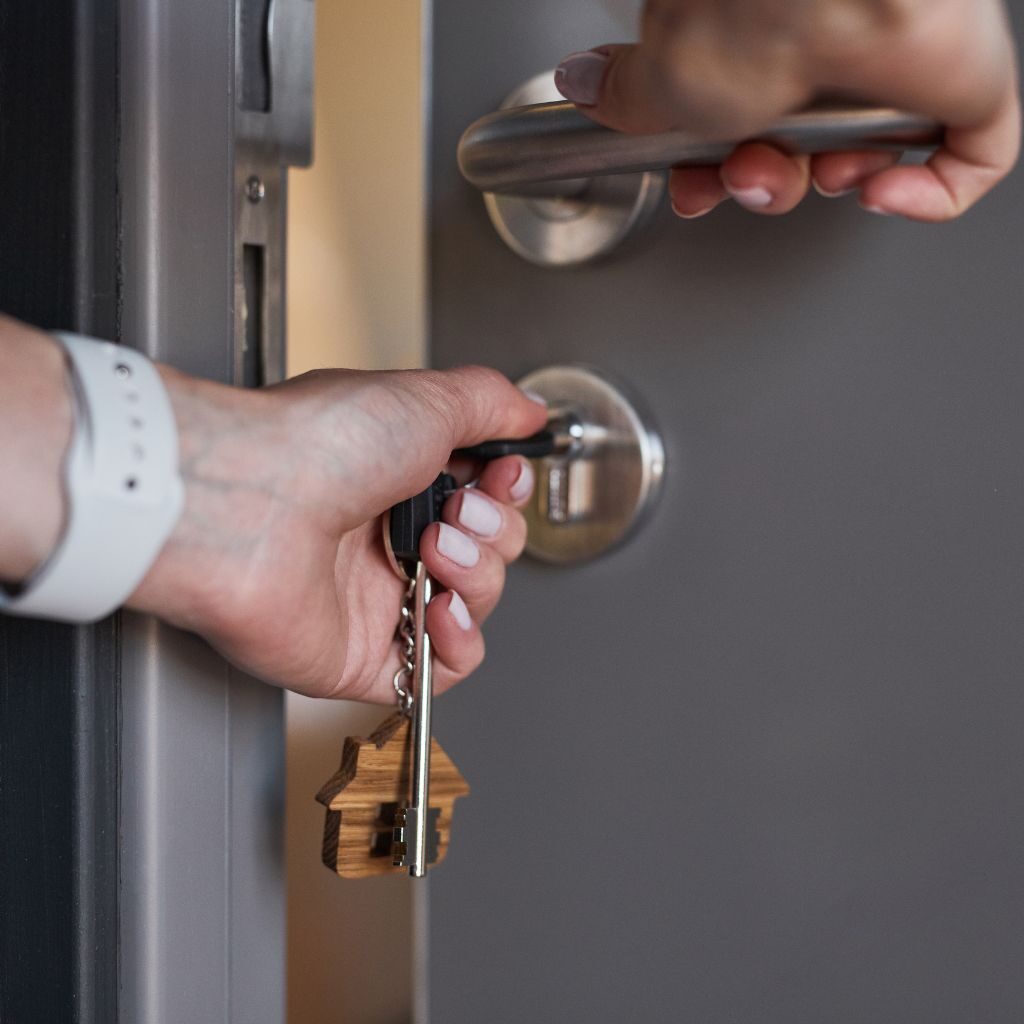 Hand die een sleutel in het cilinderslot van een moderne voordeur draait om de deur te openen.