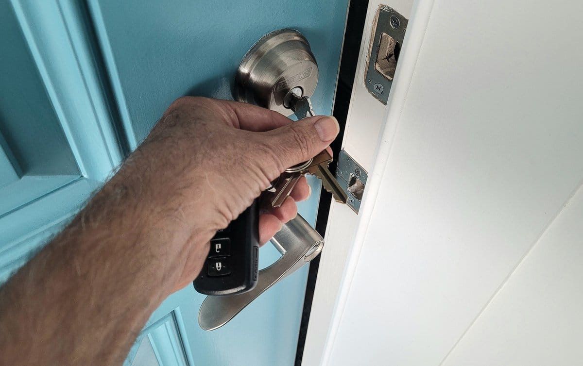 Persoon opent een witte voordeur met een sleutel in het slot en houdt de deurklink vast.